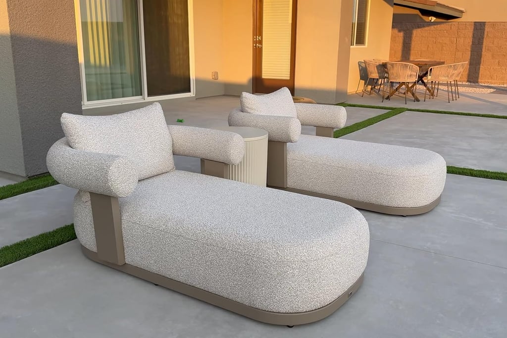 Modern outdoor chaise lounges with curved gray upholstery on a luxury concrete patio at sunset.