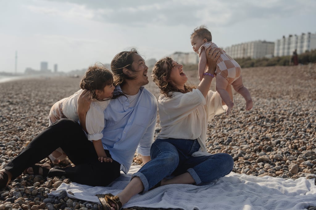 Family image on the Brighton beach laughing holding their baby in the air