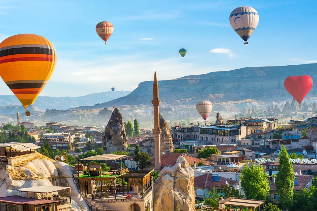 Colorful hot air balloons flying over Cappadocia town with fairy chimneys, mosque minaret, and rocky
