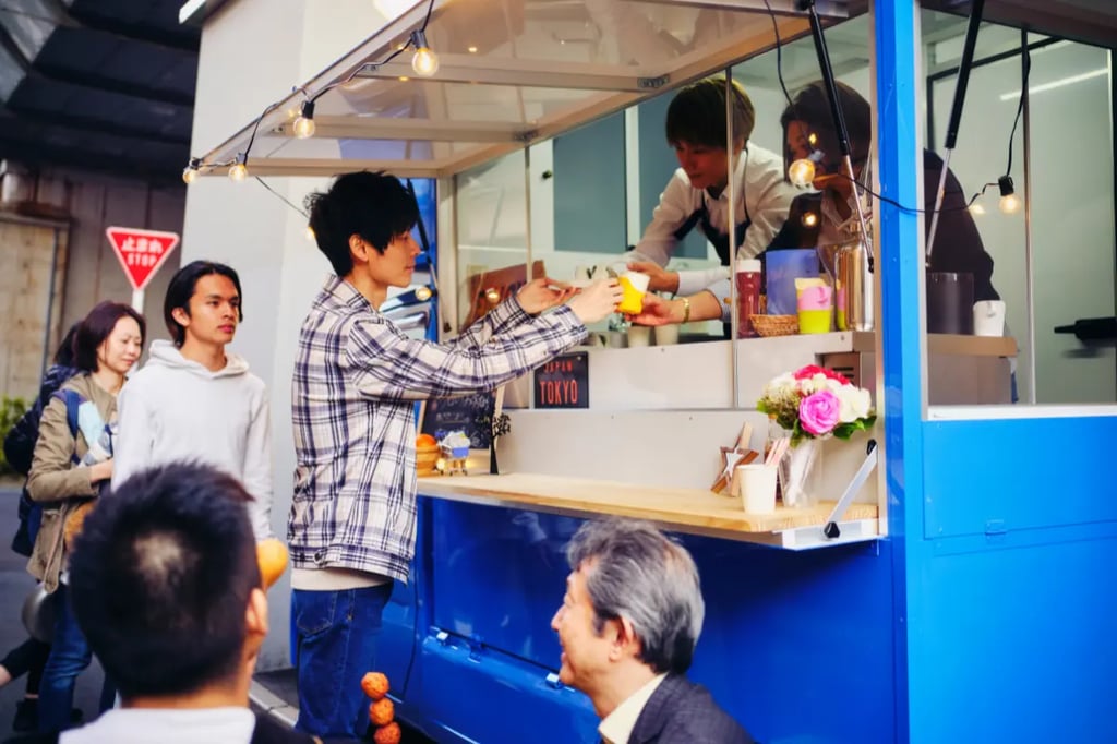 Customers ordering food at vibrant blue street food kiosk with string lights and Tokyo sign in urban