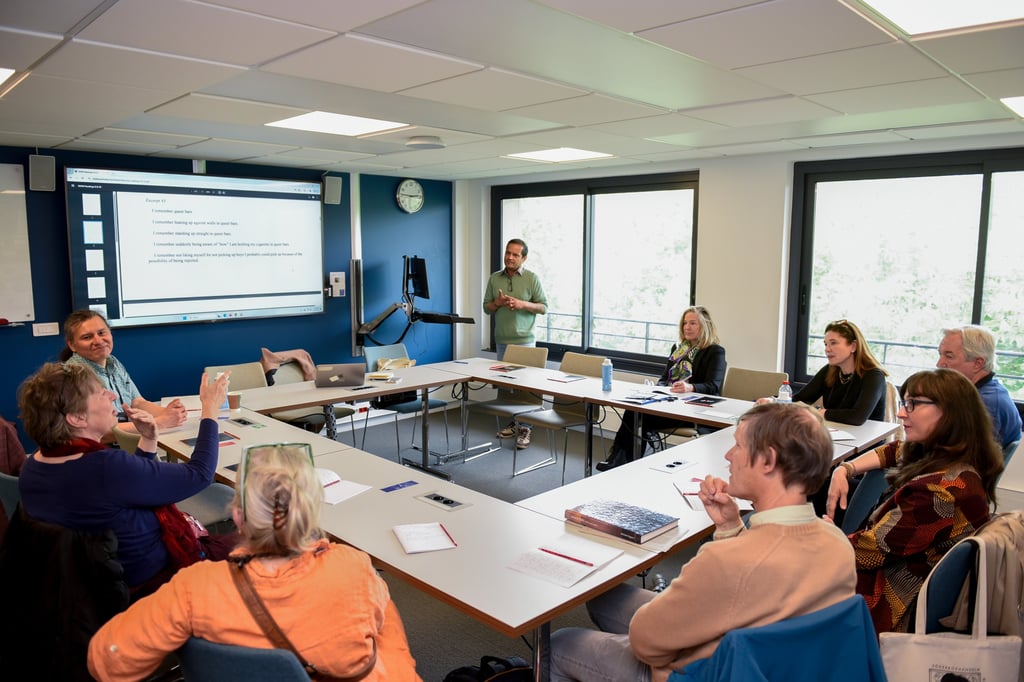 Un groupe d'adulte sont réunis autour d'une table carrée. Ils suivent la conférence d'un intervenant