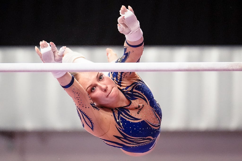 Gymnast performing a high-flying release move on the uneven bars at a gymnastics competition.