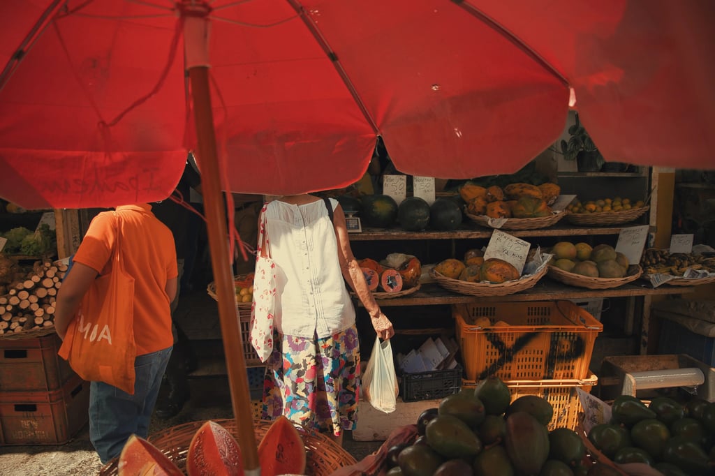 Street market scene under red umbrella showing fruit vendors and shoppers at Port Louis Central Market, Mauritius