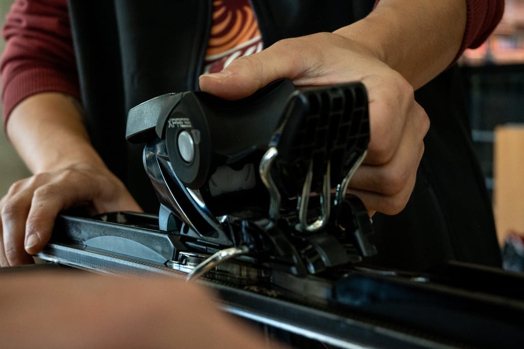 A technician's hands adjusting black Xpress ski bindings on a pair of downhill skis for safety.