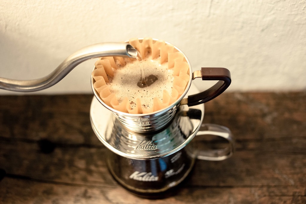 Hot water pouring from a gooseneck kettle into a Kalita Wave dripper for pour over coffee.