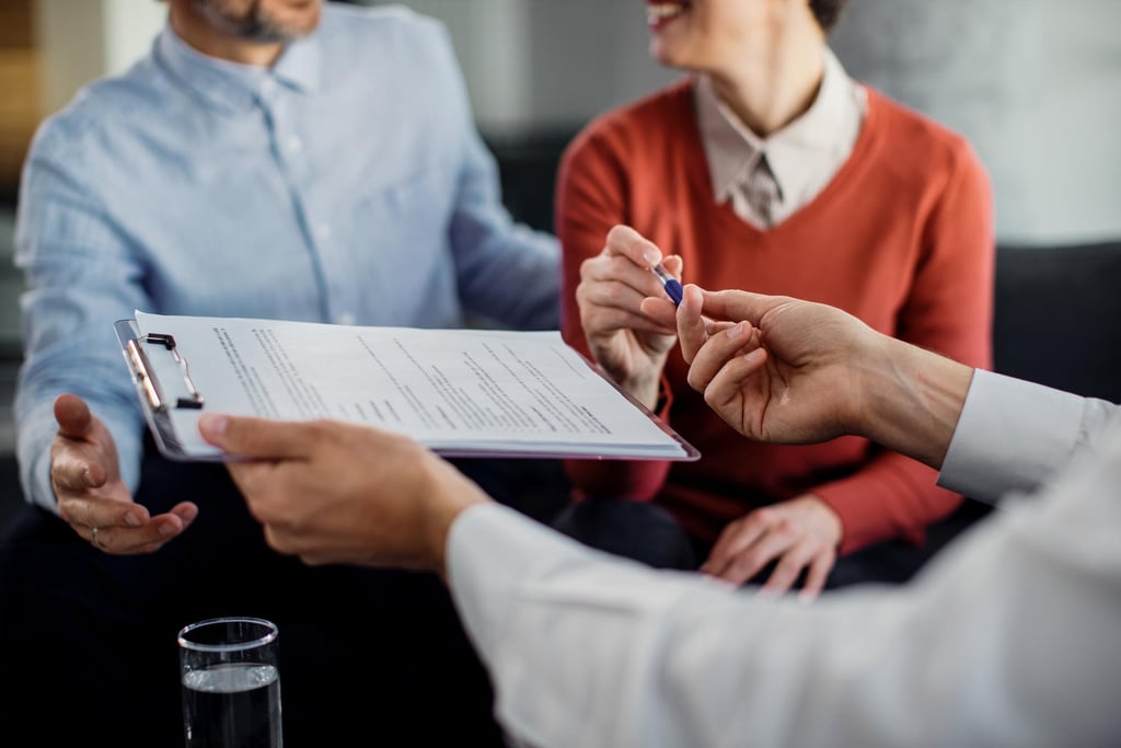 a man and woman sitting on a couch with a pen and paper signing an insurance policy
