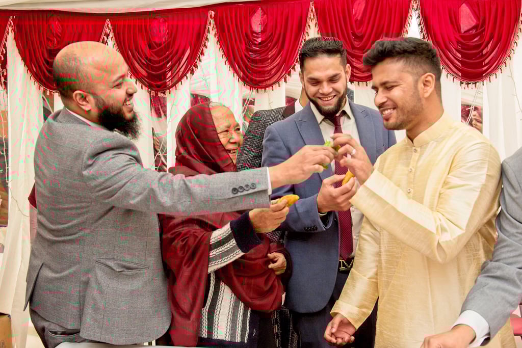 candid photo during Bengali wedding ceremony of groom's family feeding groom, all happy and laughing 