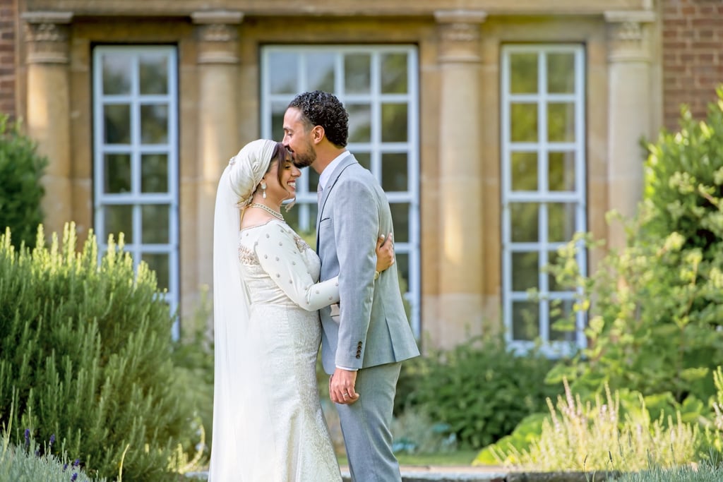 asian bride and groom outside stately home, groom kissing bride, brushes are framing the couple 