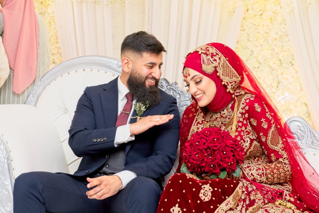 candid photo of asian bride and groom both laughing, groom in dark blue western suit, bride in traditional red dress