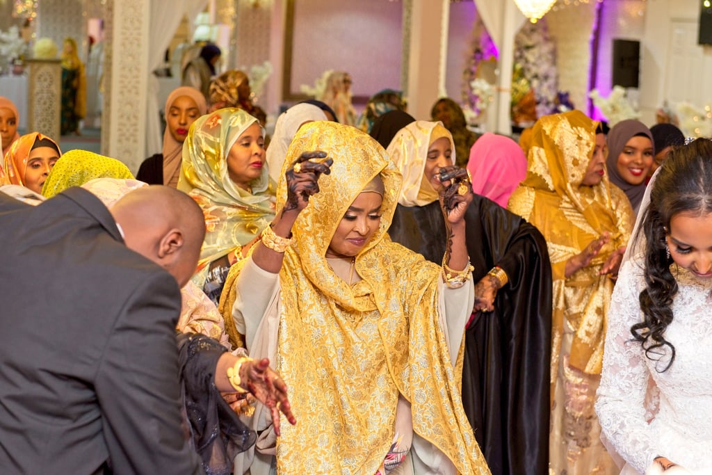 candid photo of mother Somalian bride dancing with bride and groom, all happy, wearing vibrant colours of clothing  