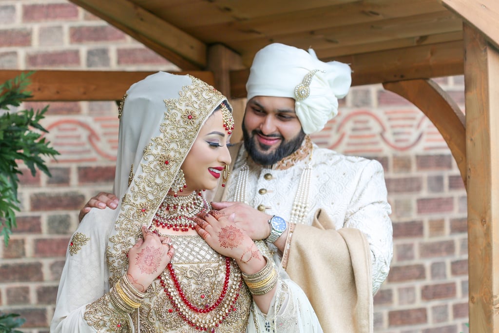 asian bride and groom, both in traditional gold and cream outfits, bride looking to side and groom looking at bride smiling  