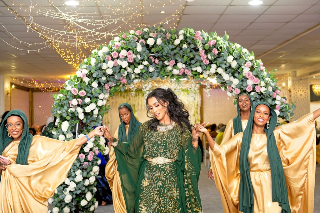 Somalian bride walking into venue with bridesmaids, all in vibrant traditional dresses, all happy and dancing  