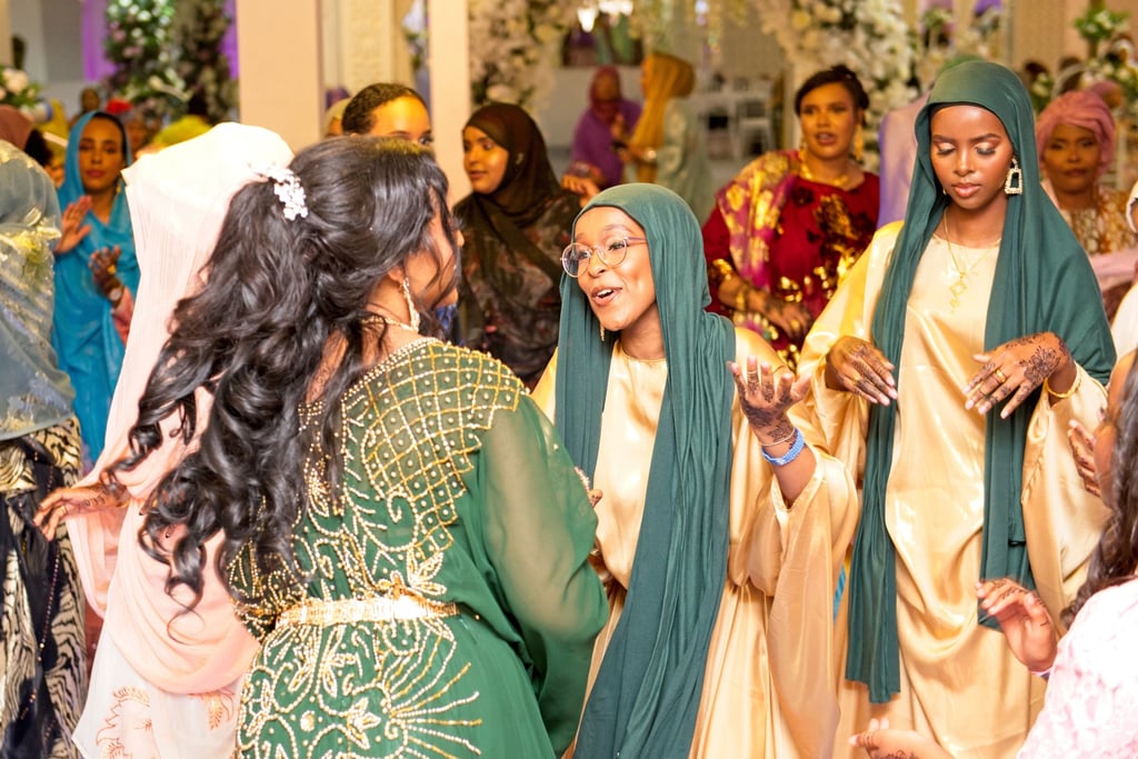 Somalian bride dancing with happy bridesmaid, both in traditional gold & green dresses 