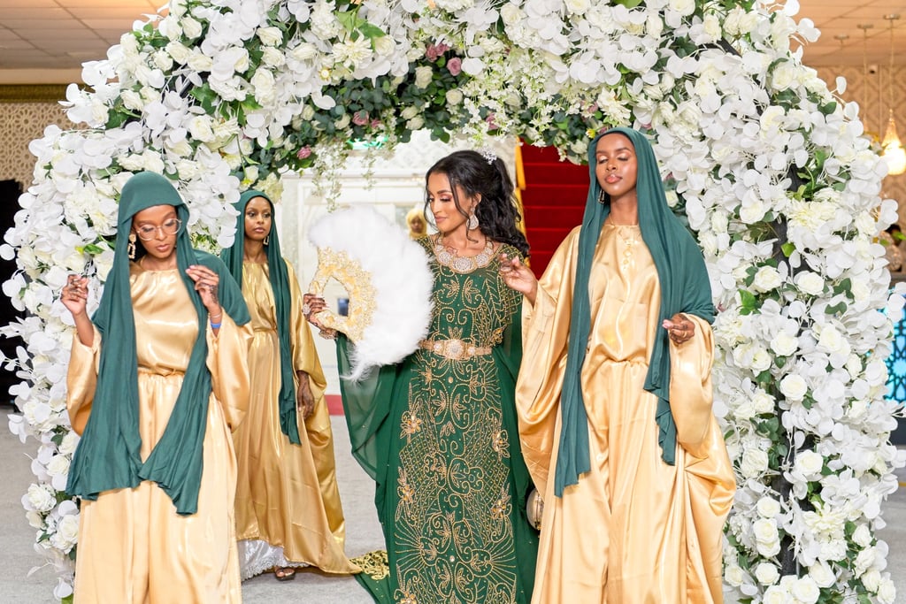 Somalian bride walking into venue with bridesmaids, all in vibrant traditional dresses, all happy and dancing  