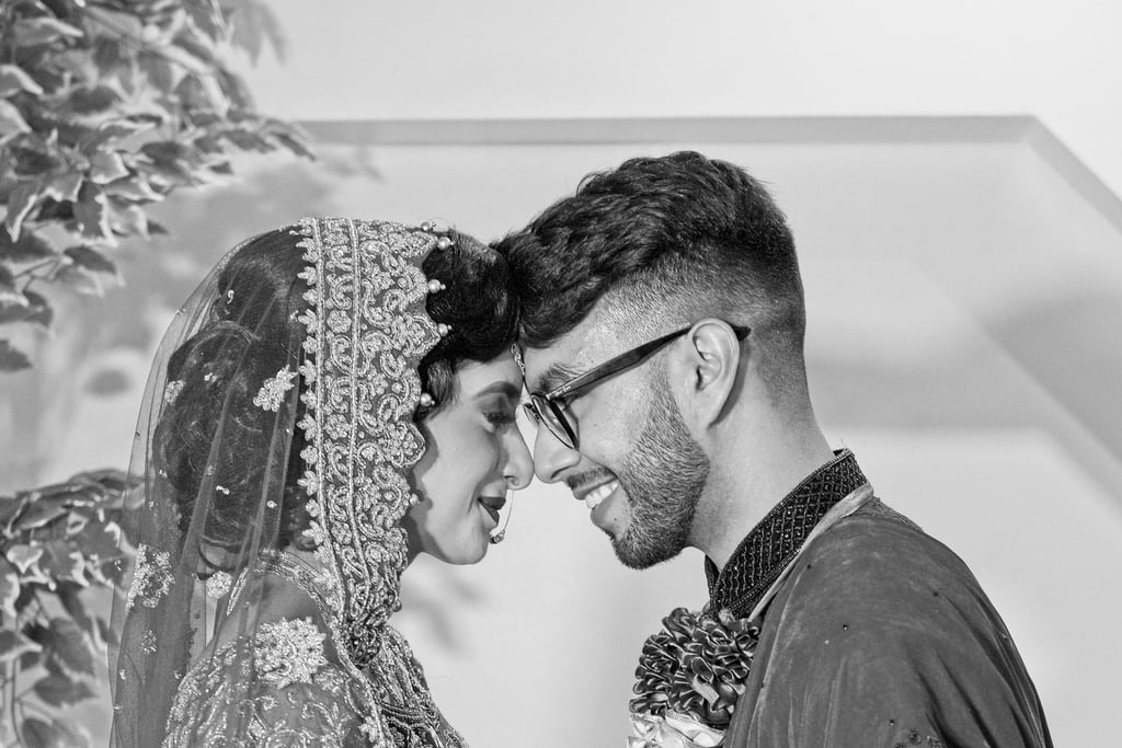 black and white photo of asian bride and groom wearing traditional wedding clothes, holding hands and foreheads touching 