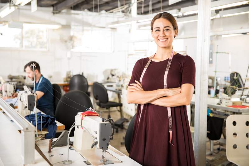 Una diseñadora de moda sonriente con una cinta métrica en la sala de costura de una fábrica de ropa.