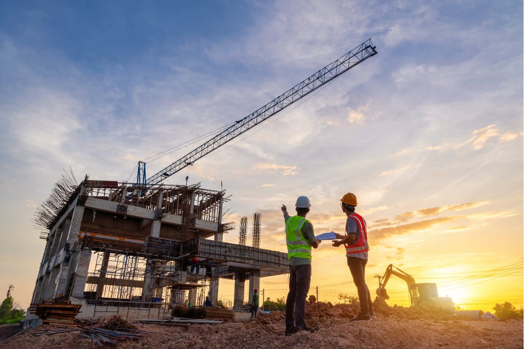 Civil engineers wearing safety helmets inspecting a building construction site at sunset with a crane.