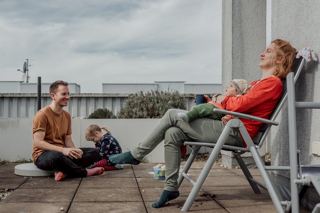 Eine junge Familie entspannt sich an einem sonnigen Tag gemeinsam auf einer  Dachterrasse.