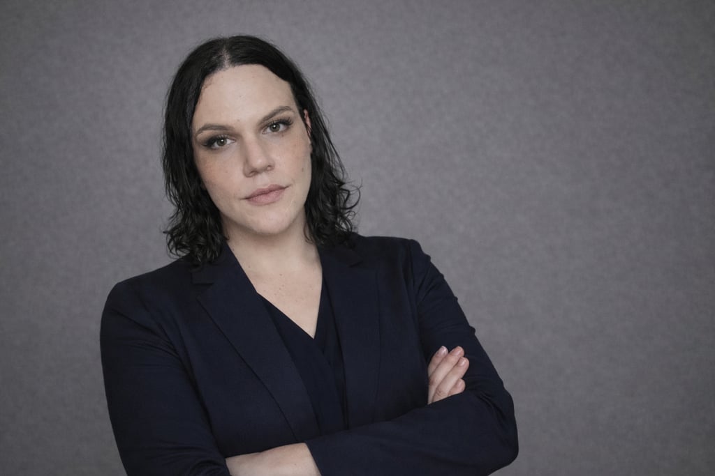 Professional portrait of a businesswoman in a dark navy blazer with arms crossed against a grey background.
