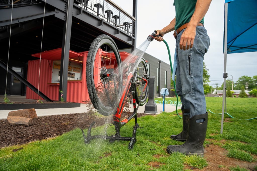 A bike flipped upside down, on the grass, with someone next to it spraying it with a hose