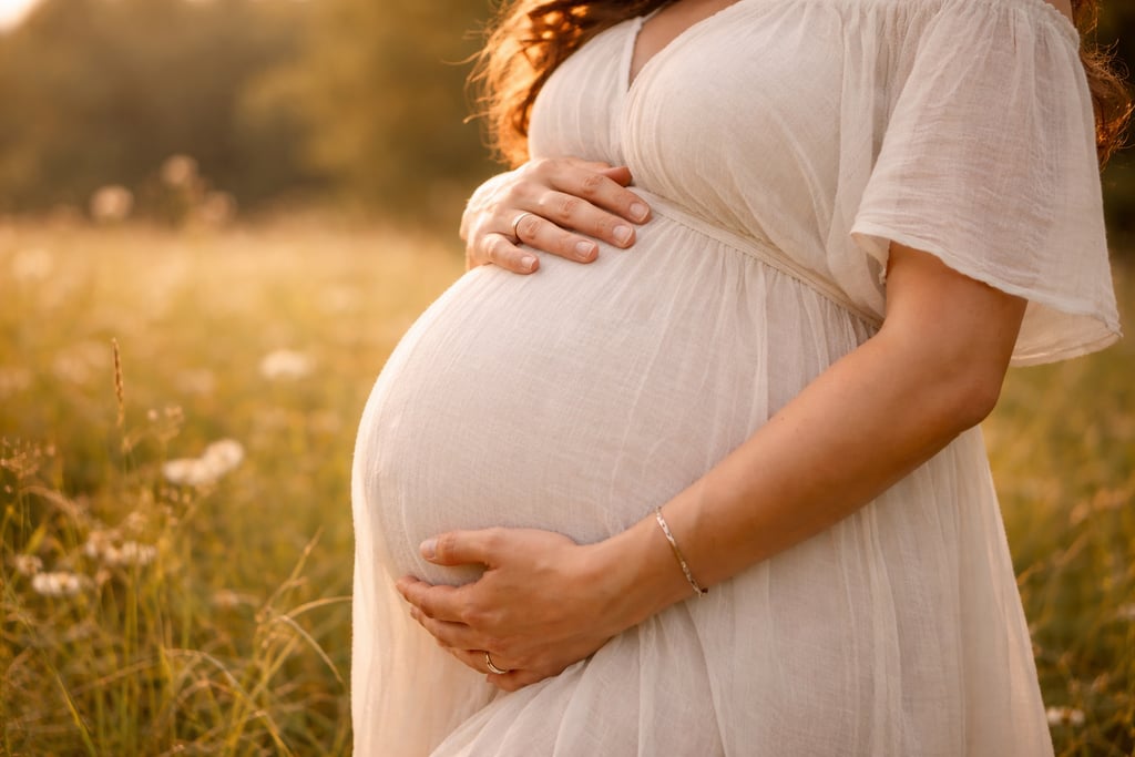 A pregnant woman in a white maternity dress cradles her baby, energetische Geburtsbegleitung