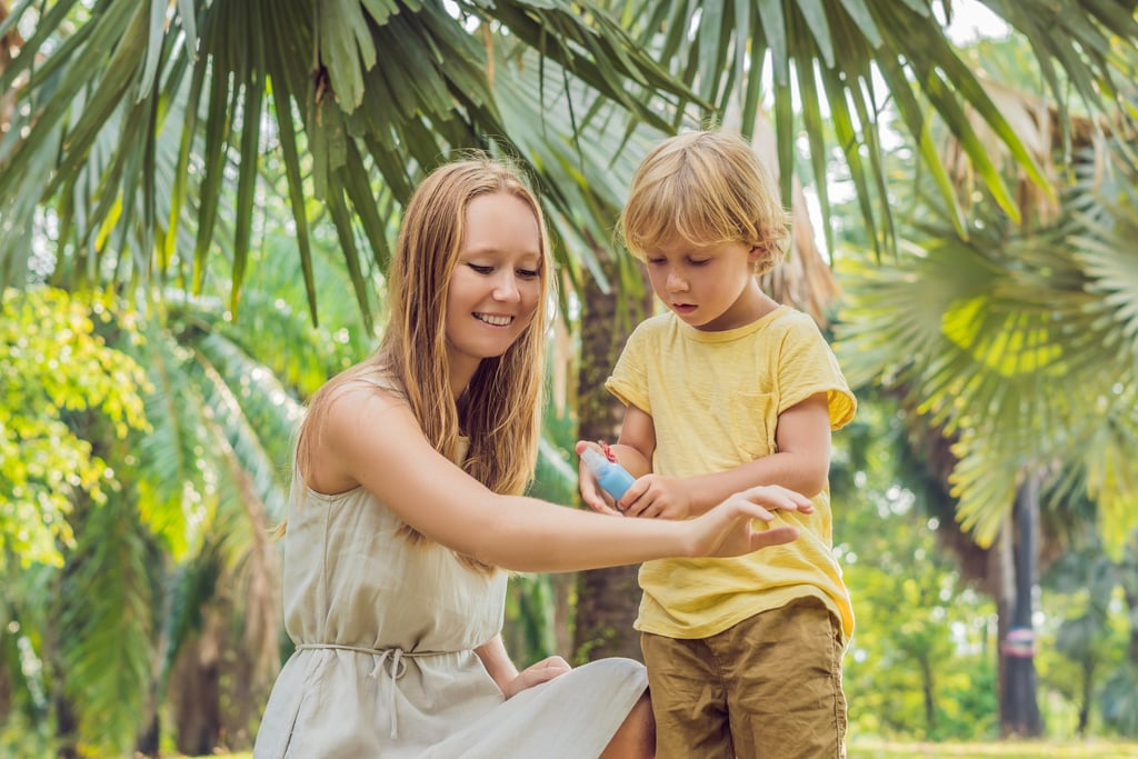 Mom helping child apply mosquito repellent in tropical outdoor setting