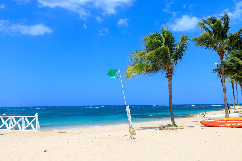 Green flag flying on a calm beach in the Dominican Republic, showing safe swimming conditions.