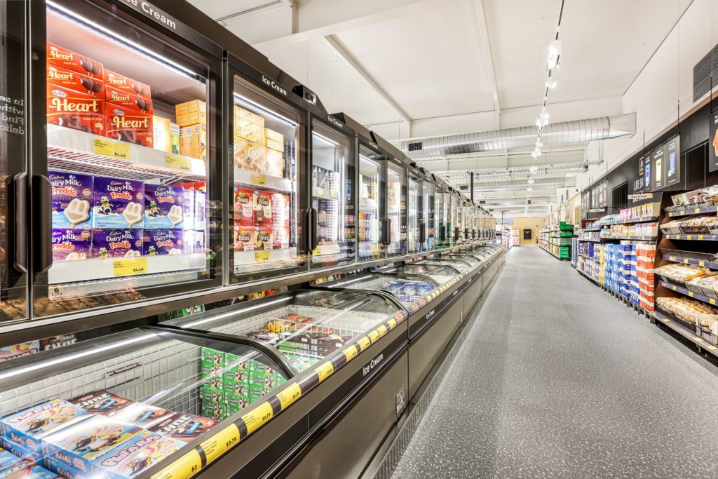 A wide grocery store aisle featuring a long row of glass-door ice cream freezers and frozen food displays.