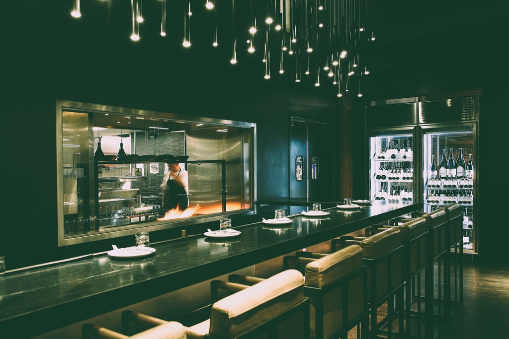 Modern upscale restaurant interior featuring an open kitchen, bar seating, and hanging pendant lights.