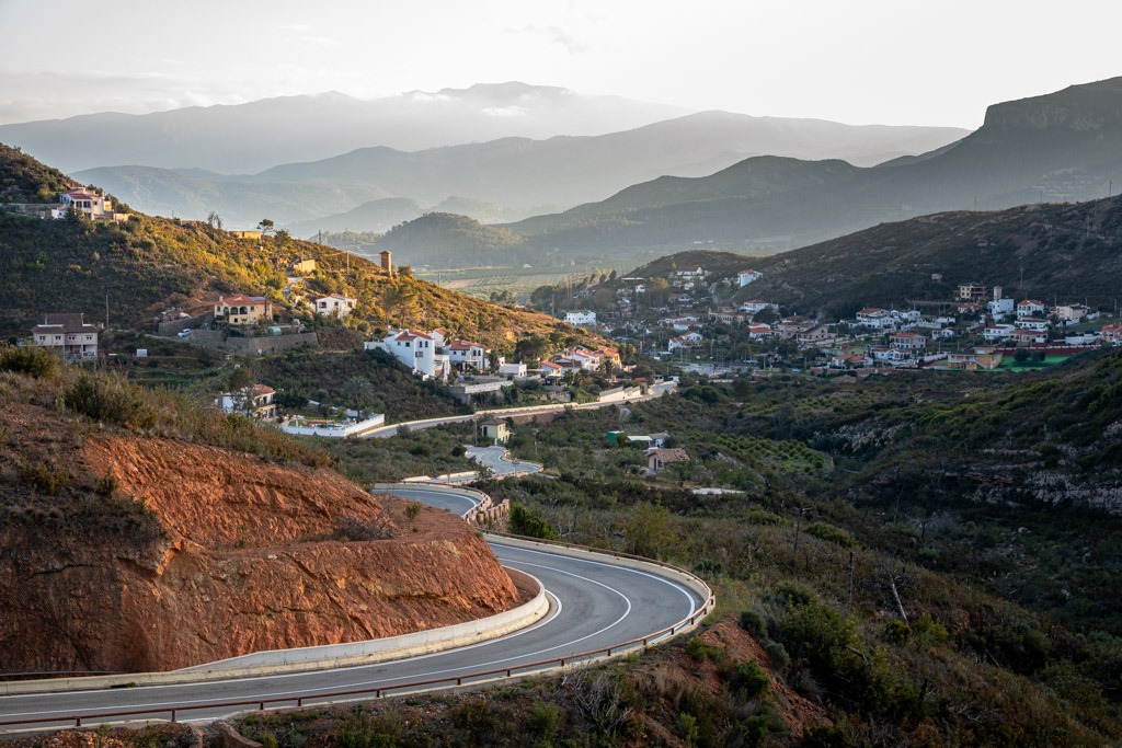 Winding road leading towards a Spanish mountain village and fading mountains in the background