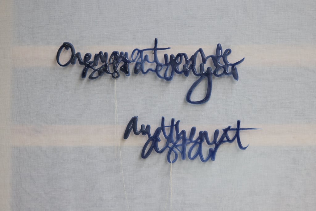 A glass sculpture with semi-abstract text hangs on a wall. its 2 sections are joined by silver chain