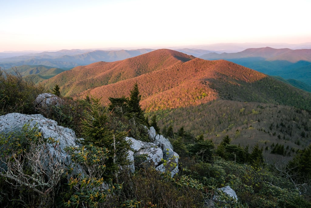 Sunset over Blue Ridge Mountains landscape with rocky peak and green forest ridges.