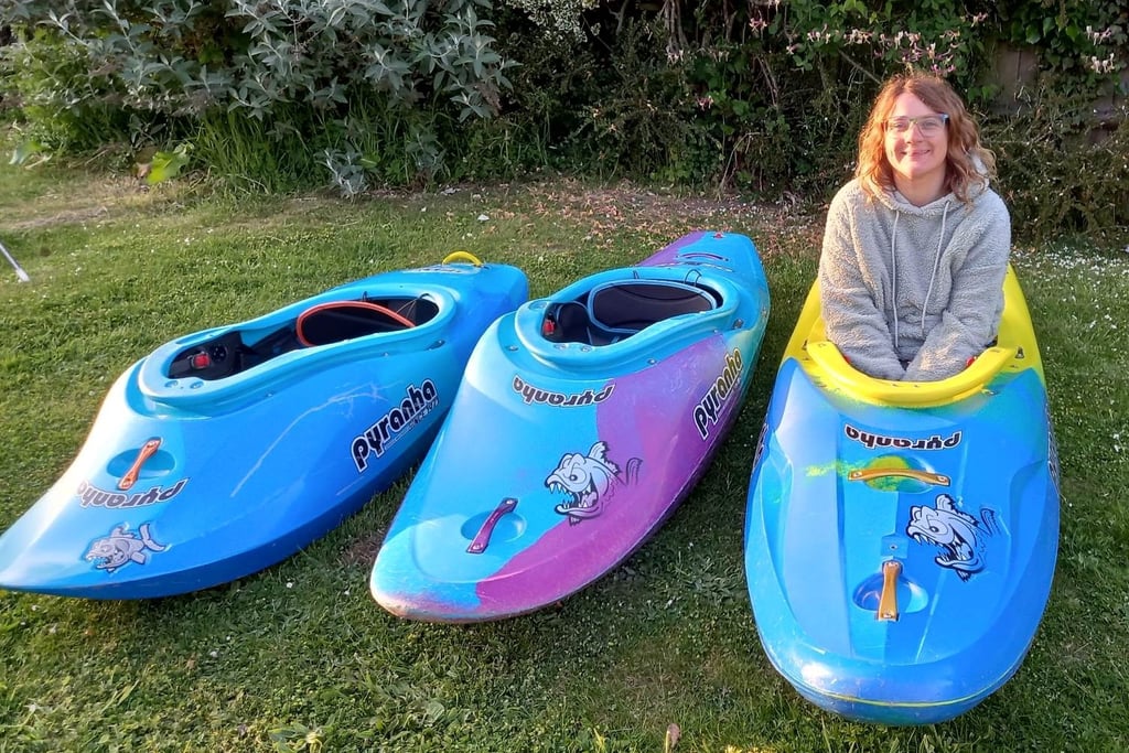 a woman sitting on a lawn with three kayaks