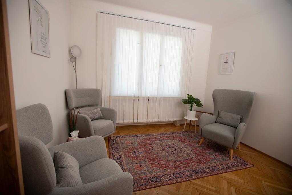 Gemütlicher Therapieraum mit Sesseln, Teppich und hellem Tageslicht vom Fenster.