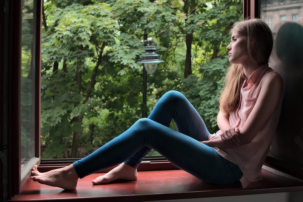 a woman sitting on a window sill with her feet on the floor