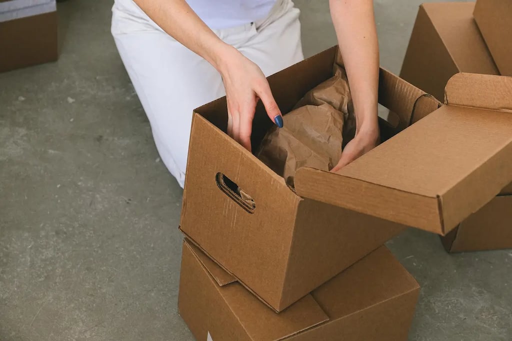 A person packing cardboard shipping boxes with brown paper for safe moving and delivery.