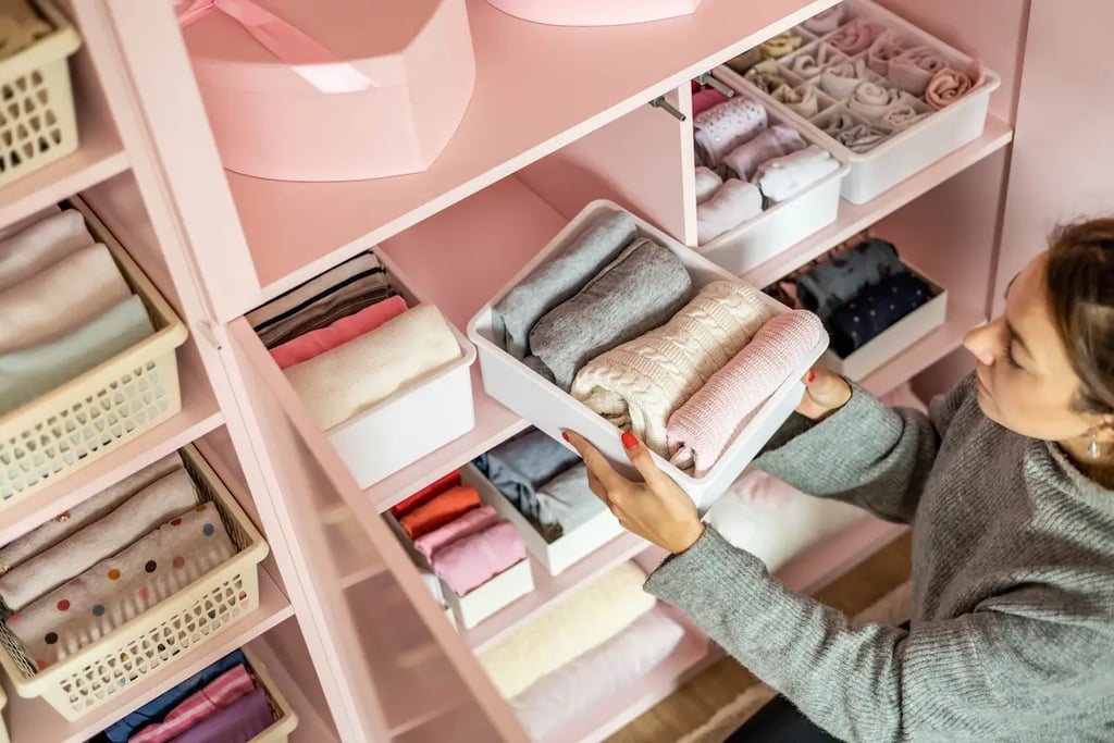 Woman organizing a pink closet using white storage bins to fold and sort sweaters and clothes.