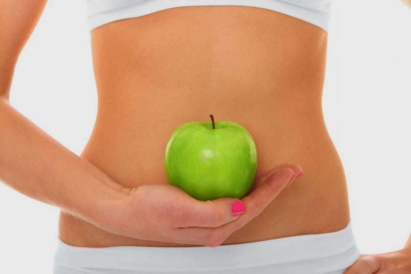 Person holding a green apple at the abdomen, symbolising Chi Nei Tsang focus on digestive organ health and energy flow