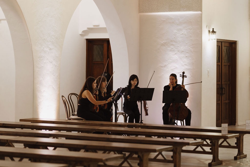 Professional string quartet performing live music for a wedding ceremony in a chapel.