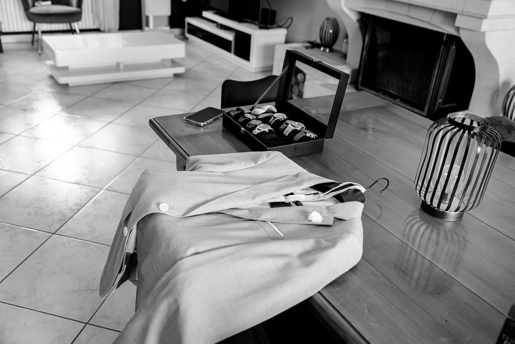 Photo en noir et blanc d'un blazer pour homme et d'un coffret de montre de luxe posés sur une table 