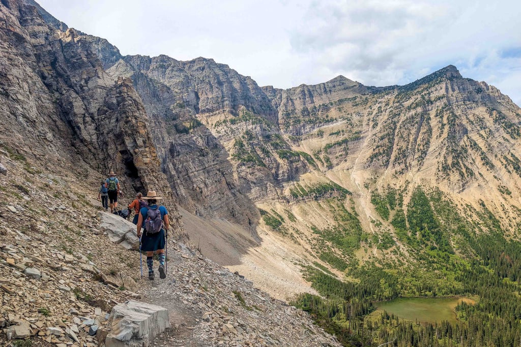 Hikers walking along a narrow cliff section on the Crypt Lake Trail in Waterton Lakes National Park.