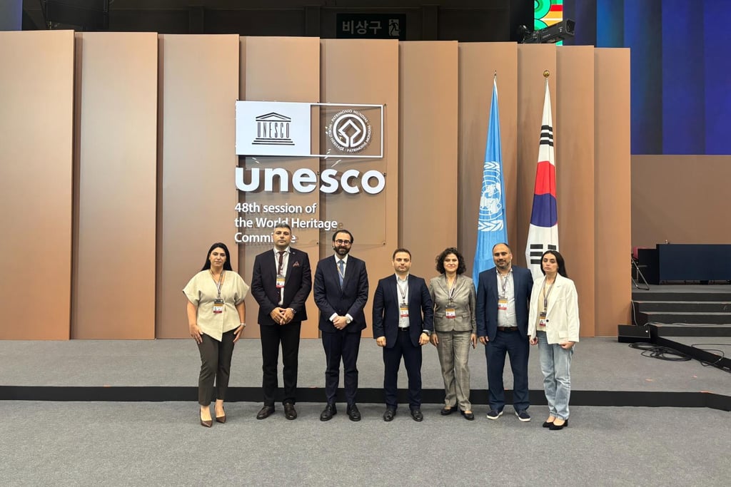 Delegates standing at the UNESCO 48th session of the World Heritage Committee with international flags.