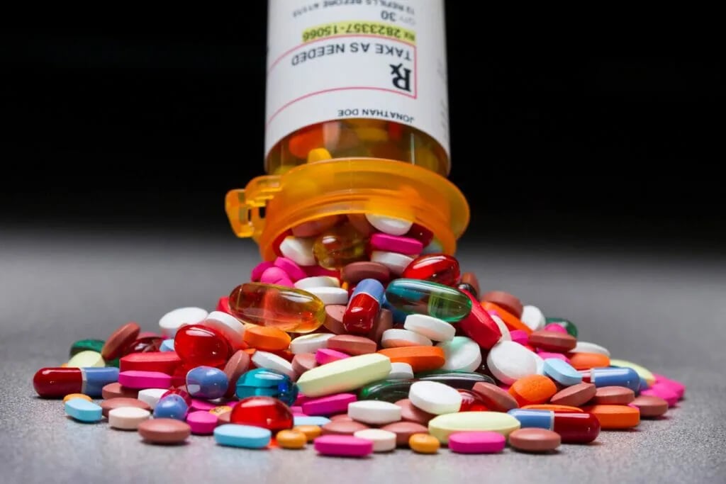 A variety of colorful prescription pills and capsules spilling from an orange medication bottle.