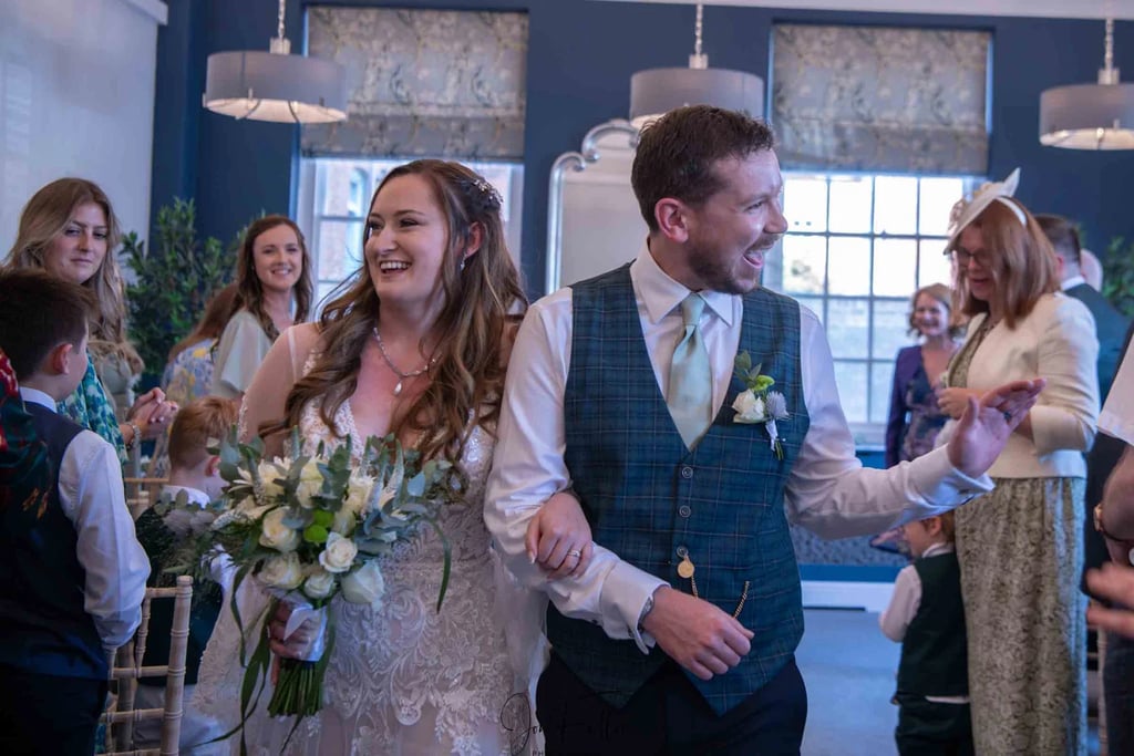 Smiling bride and groom walking down the aisle after an indoor wedding ceremony with guests.