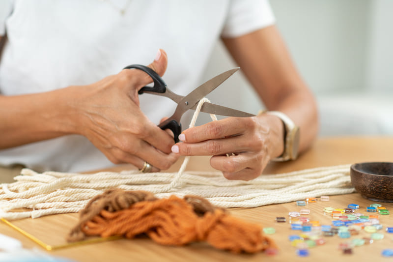 Persona cortando cordón de algodón blanco para proyecto de macramé artesanal hecho a mano.