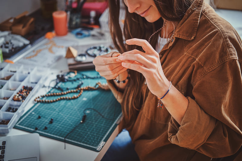 Una diseñadora de joyas elaborando un collar artesanal con cuentas en una estación de trabajo