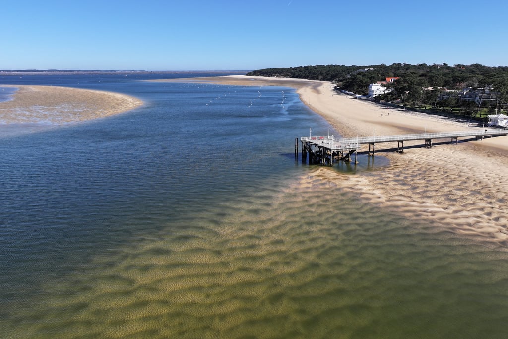 Vue aérienne d'une plage ensoleillée et d'un quai en bois s'étendant dans l'eau du bassin d'Arcachon