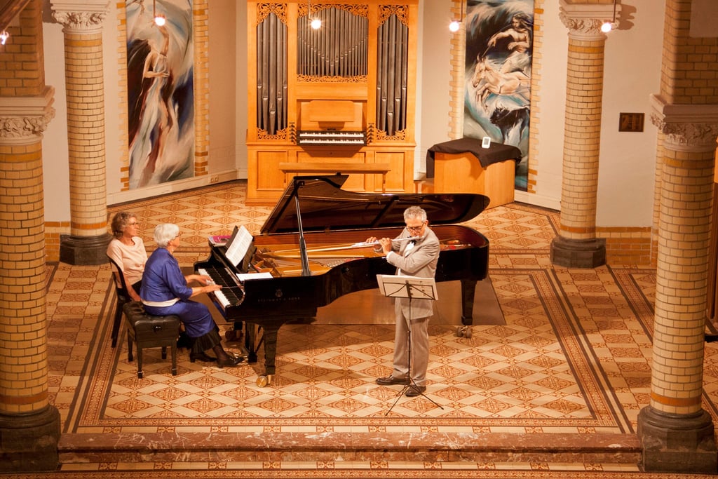 Classical music concert featuring a flutist and pianist performing together in a chapel with a pipe organ.