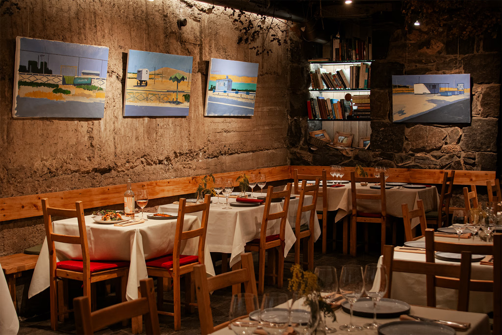 Rustic restaurant interior with white tablecloth settings, stone walls, and oil paintings.