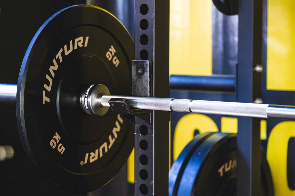 A barbell with a 5kg Tunturi bumper plate resting on a black steel power rack in a gym.